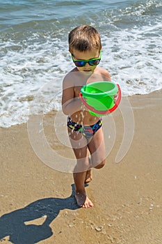 The boy is playing at sea with a bucket. Little boy having beach fun