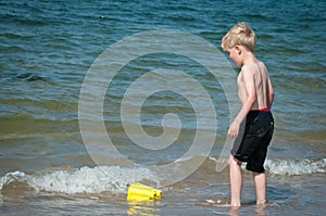 Boy playing in the sea with a yellow buckey