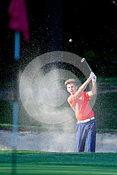 Boy playing a shot from the bunker on a golf course.