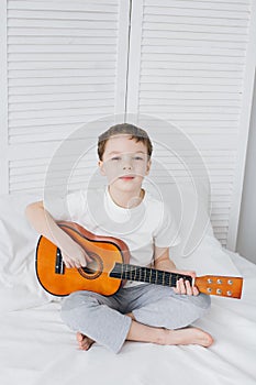 Boy playing a small guitar sitting on the bed