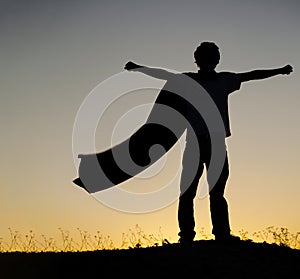 Boy playing superheroes on the sky background, teenage hero in cloak on a hill