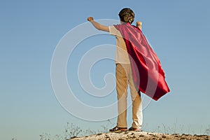 Boy playing superheroes on the sky background, teenage superhero