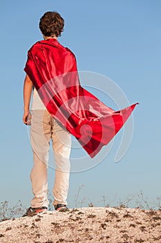 Boy playing superheroes on the sky background, teenage superhero