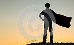 Boy playing superheroes on the sky background, teenage superhero in a red cloak on hill