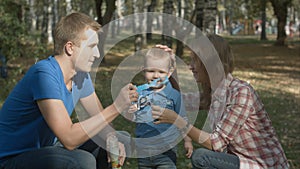 Boy is playing together with his parents. They are playing with soap-bubbles.