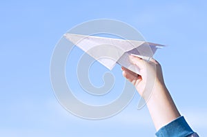 A boy is playing with a toy paper airplane against the blue sky in the field