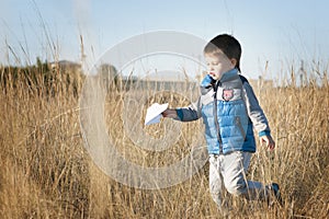 A boy is playing with a toy paper airplane against the blue sky in the field