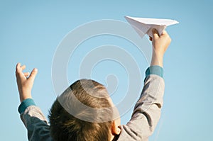 A boy is playing with a toy paper airplane against the blue sky in the field