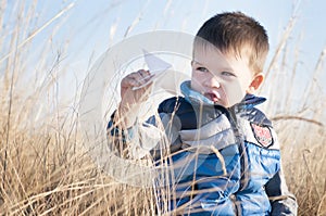 A boy is playing with a toy paper airplane against the blue sky in the field