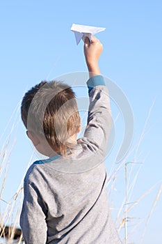 A boy is playing with a toy paper airplane against the blue sky in the field