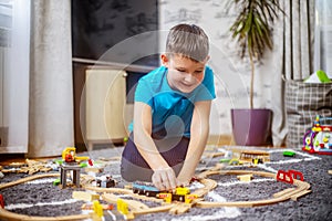 Boy playing with toy train with wooden rails while sitting on floor at home