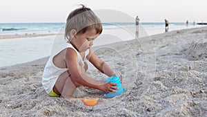 Boy playing with toys on the beach building beads and turrets smiling at someone behind the scenes on summer vacation