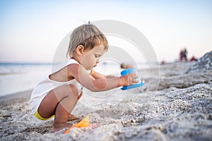 Boy playing with toys on the beach building beads and turrets smiling at someone behind the scenes on summer vacation