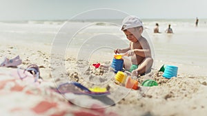 Boy playing with toys on the beach building beads and turrets smiling at someone behind the scenes on summer vacation