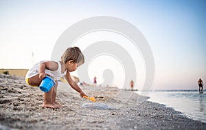 Boy playing with toys on the beach building beads and turrets smiling at someone behind the scenes on summer vacation