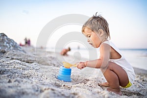 Boy playing with toys on the beach building beads and turrets smiling at someone behind the scenes on summer vacation