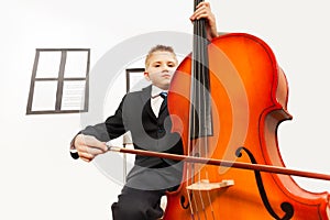 Boy playing violoncello sitting on the chair