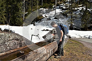Boy playing with the water in wooden water-trough surrounded by snow near by tourist path heading directly towards to Murg lakes