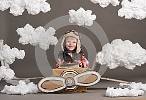 The boy plays in an airplane made of cardboard box and dreams of becoming a pilot, clouds of cotton wool on a gray background