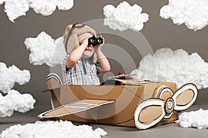 The boy plays in an airplane made of cardboard box and dreams of becoming a pilot, clouds from cotton wool on a gray background, r