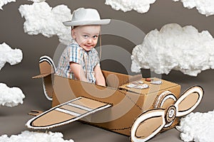 The boy plays in an airplane made of cardboard box and dreams of becoming a pilot, clouds from cotton wool on a gray background, r