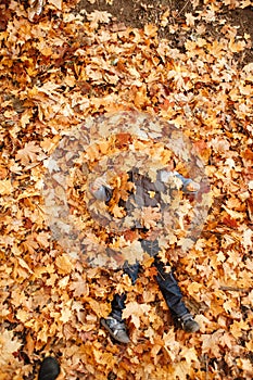 The boy plays in the autumn park. Dug into fallen leaves