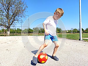 A boy plays ball at the playground. Asphalt sports court. A child in a white t-shirt. Toddler with blond hair, blond, 7 years old