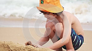 A boy plays on the beach in the sand. Child building sand castles close-up.