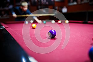 Boy plays billiard or pool in club. Young Kid learns to play snooker. Boy with billiard cue strikes the ball on table.