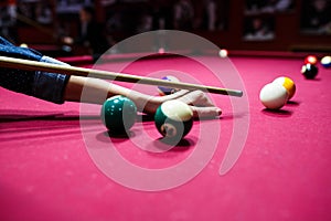 Boy plays billiard or pool in club. Young Kid learns to play snooker. Boy with billiard cue strikes the ball on table.