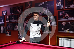 Boy plays billiard or pool in club. Young Kid learns to play snooker. Boy with billiard cue strikes the ball on table.