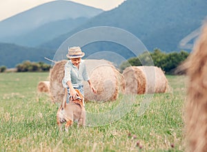 Boy plays with dog on the field with hayroll