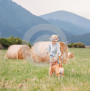 Boy plays with dog on the field with hayroll