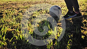 A boy plays football with a ball. Children's legs hit the ball in slow motion, the beauty of the sun's rays.