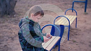 Boy plays a game on his mobile phone sitting in the Park on a bench.