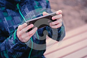 Boy plays a game on his mobile phone sitting in the Park on a bench. Close-up boy`s hands.