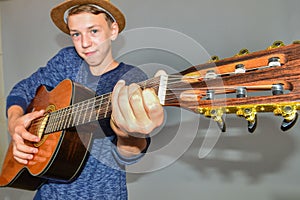 A boy plays the guitar on a gray background in the studio, wide-angle close-up photo