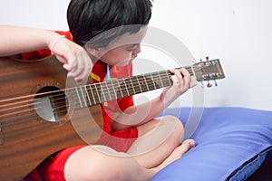 The boy plays the guitar with his left hand, a song by himself, on the sofa, in the bedroom, reading the sheet music