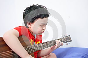 The boy plays the guitar with his left hand, a song by himself, on the sofa, in the bedroom, reading the sheet music