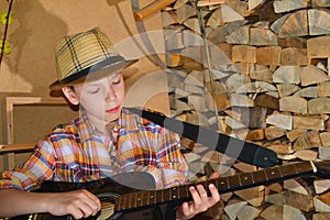 The boy plays the guitar and takes chords, dombra on the background of the firewood in the village