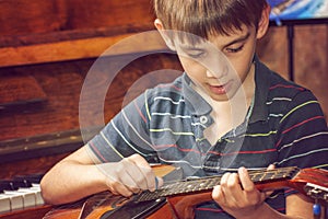 The boy plays the guitar and takes chords, dombra on the background of the piano.