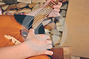 The boy plays the guitar and takes the chords to the dombra, in the background the wood in the village.