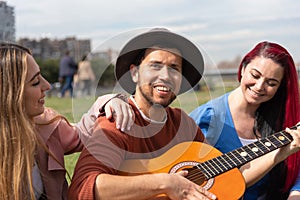 A boy plays the guitar together with two girls in a city park