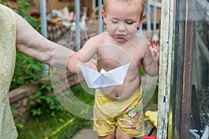 A boy plays with paper boat in the water barrel