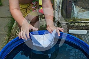 A boy plays with paper boat in the water barrel in the garden