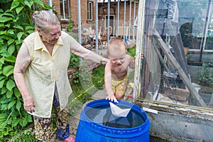 A boy plays with paper boat in the water barrel in the garden