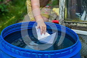 A boy plays with paper boat in the water barrel in the garden