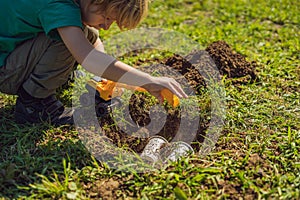 The boy plays recycling. He buries plastic disposable dishes and biodegradable dishes