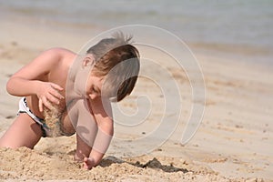 The boy plays sand on seacoast