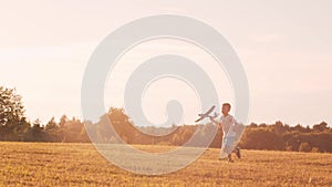 Boy plays with a toy plane in a field at sunset. The concept of childhood, freedom and inspiration.